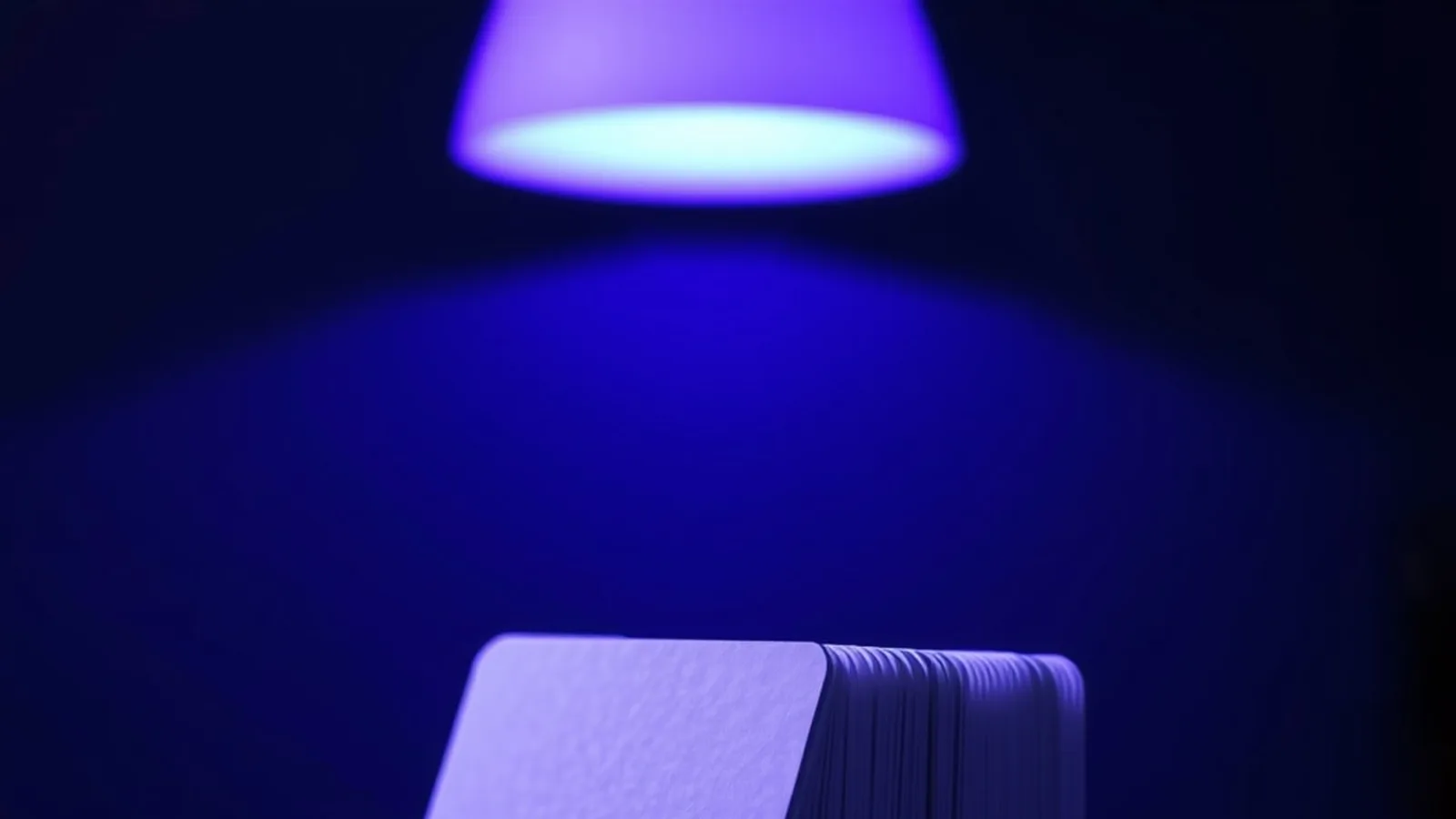 A tall stack of blank plastic cards on a dark counter under the violet glow of an ultraviolet lamp